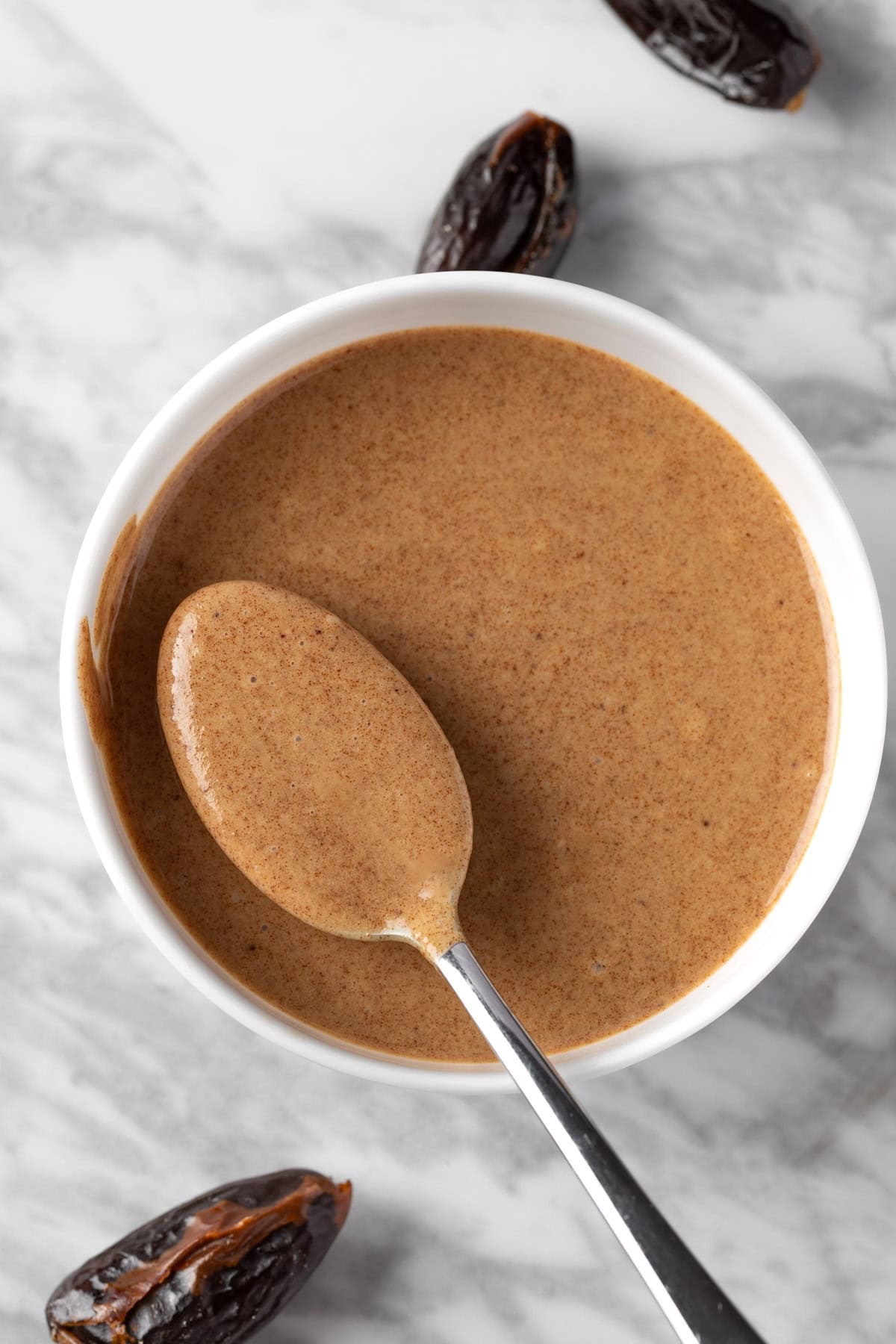 Overhead view of a spoonful of Balsamic Date Vinaigrette in a white bowl.