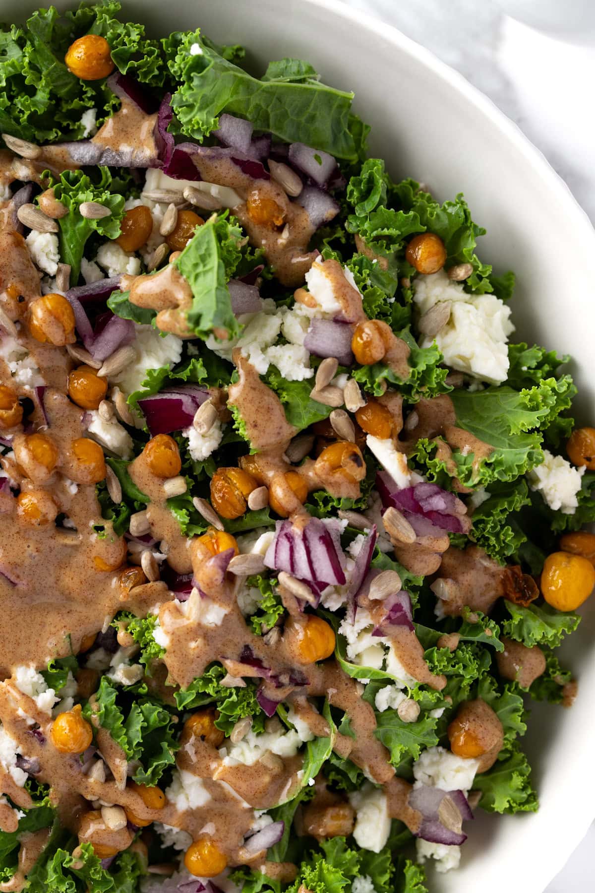 A salad with kale, feta, chickpeas, red onions with balsamic date vinaigrette drizzled on top.