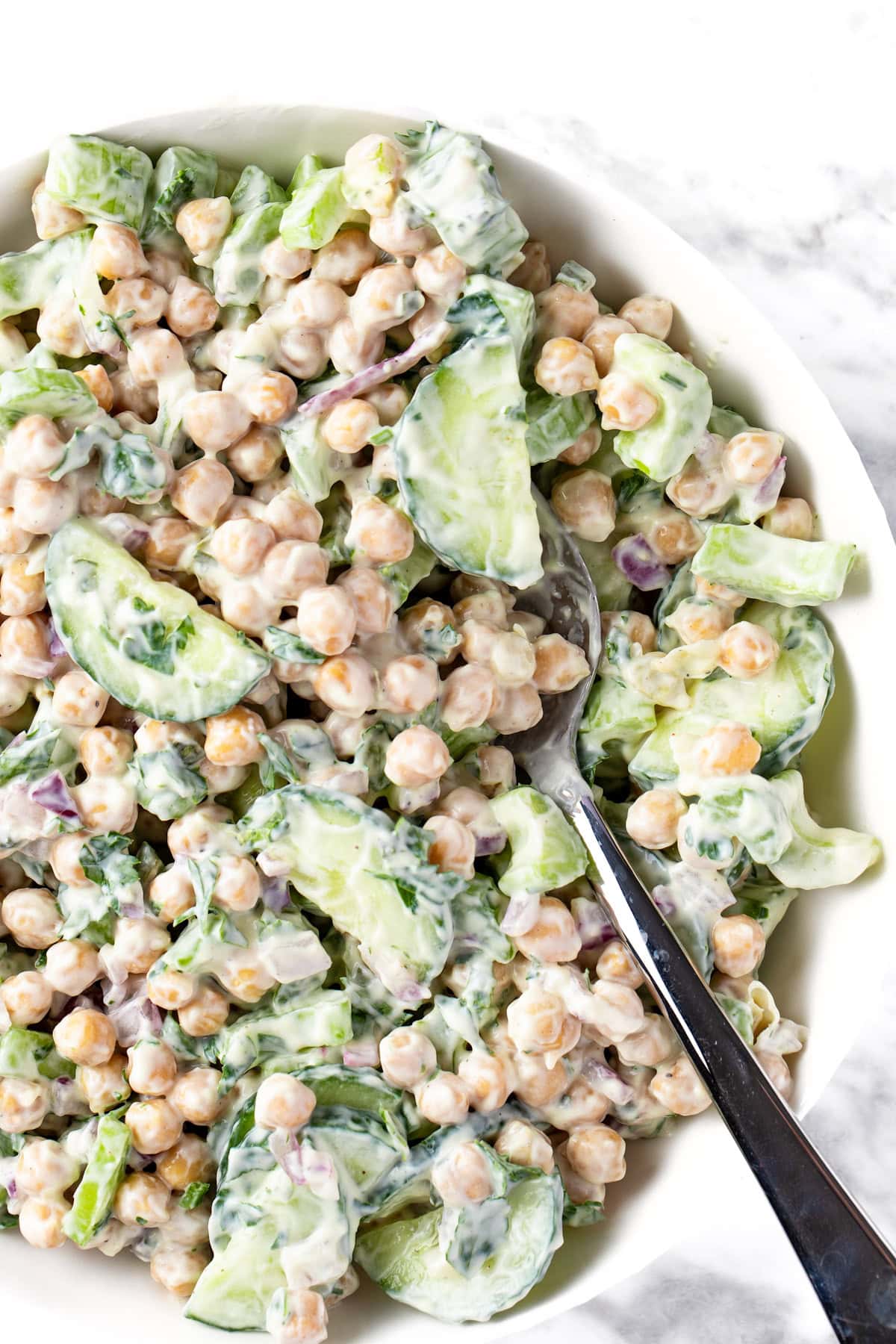 A bowl of Creamy Chickpea Salad made with chickpeas, cucumbers, red onions and parsely.