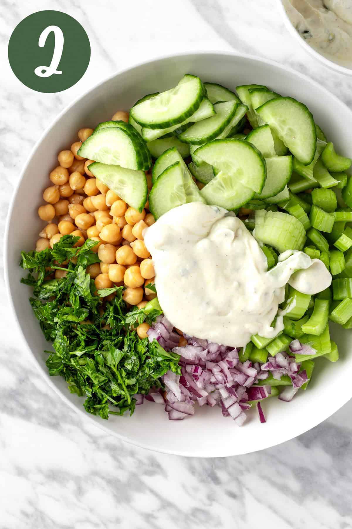 The salad ingredients in a large white bowl with a dollop of creamy dressing on top.