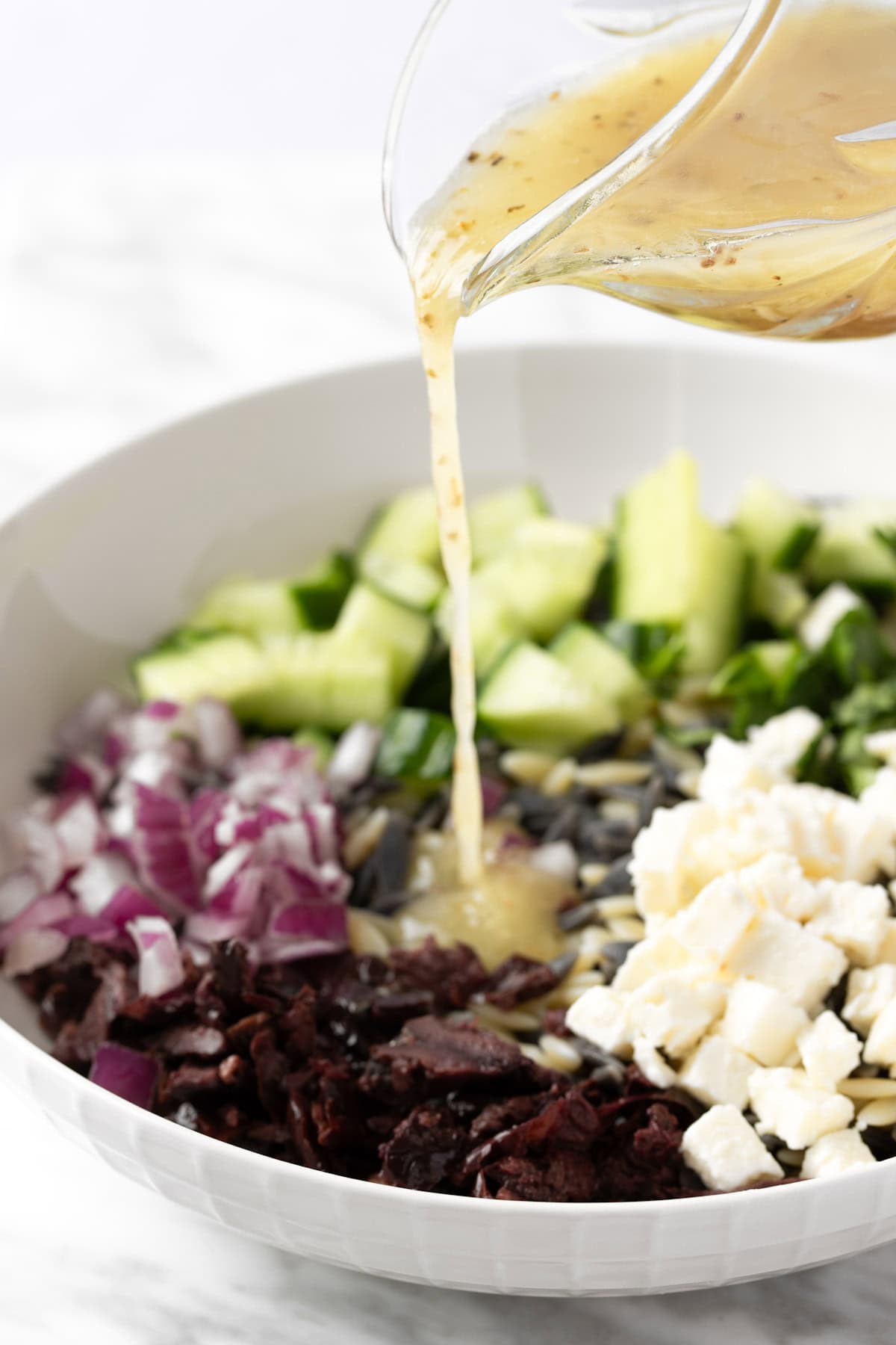 Pouring the lemon vinaigrette onto a Greek orzo salad.