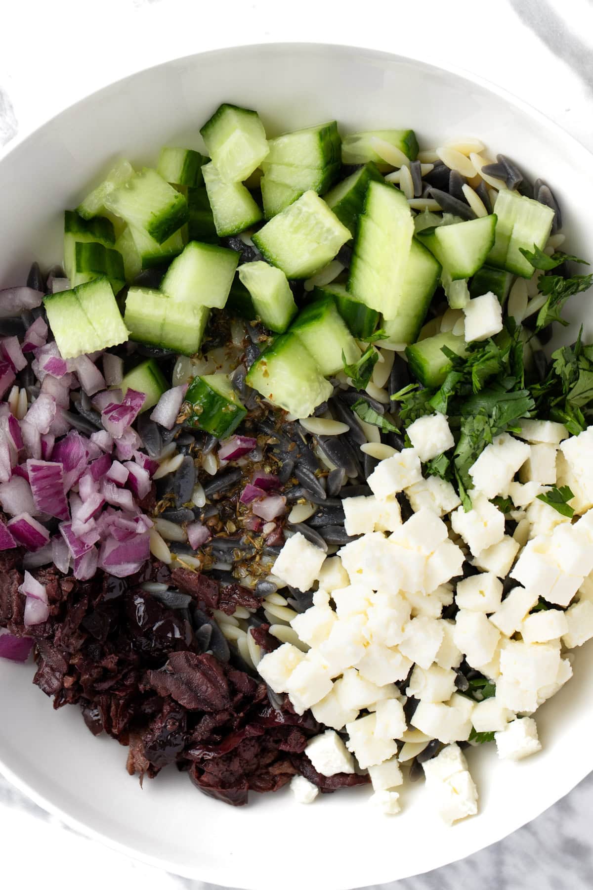 An orzo pasta salad with feta, olive, red onion, cucumber and parsley.