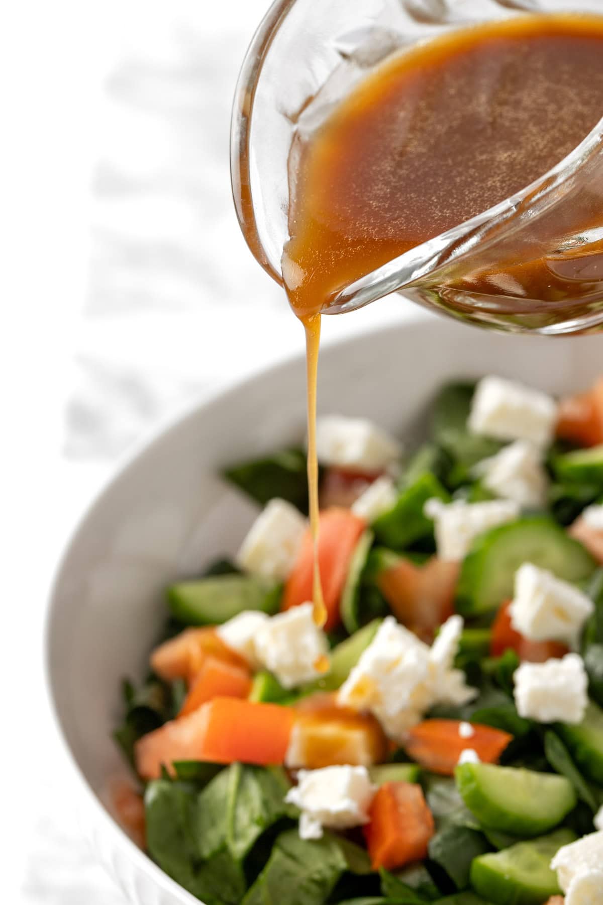 Pouring the dressing on top of a salad with spinach, cucumbers, feta and tomato.