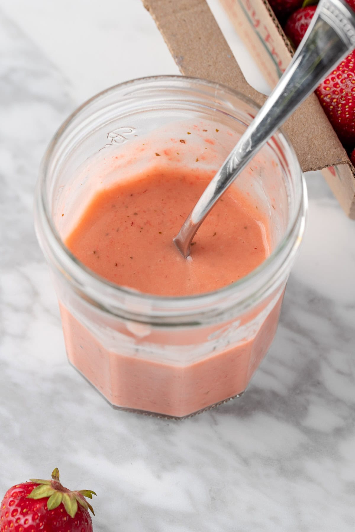 A open mason jar filled with pink strawberry basil vinaigrette.