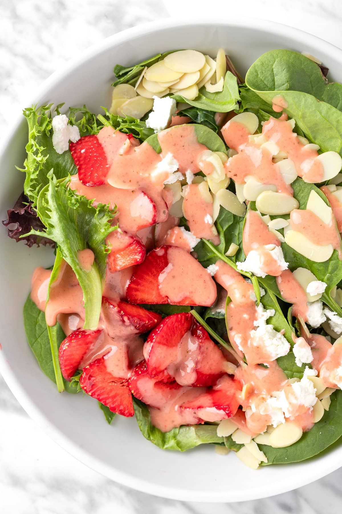 A strawberry spinach salad with almonds topped with a strawberry vinaigrette dressing.