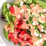 A strawberry spinach salad with almonds topped with a strawberry vinaigrette dressing.