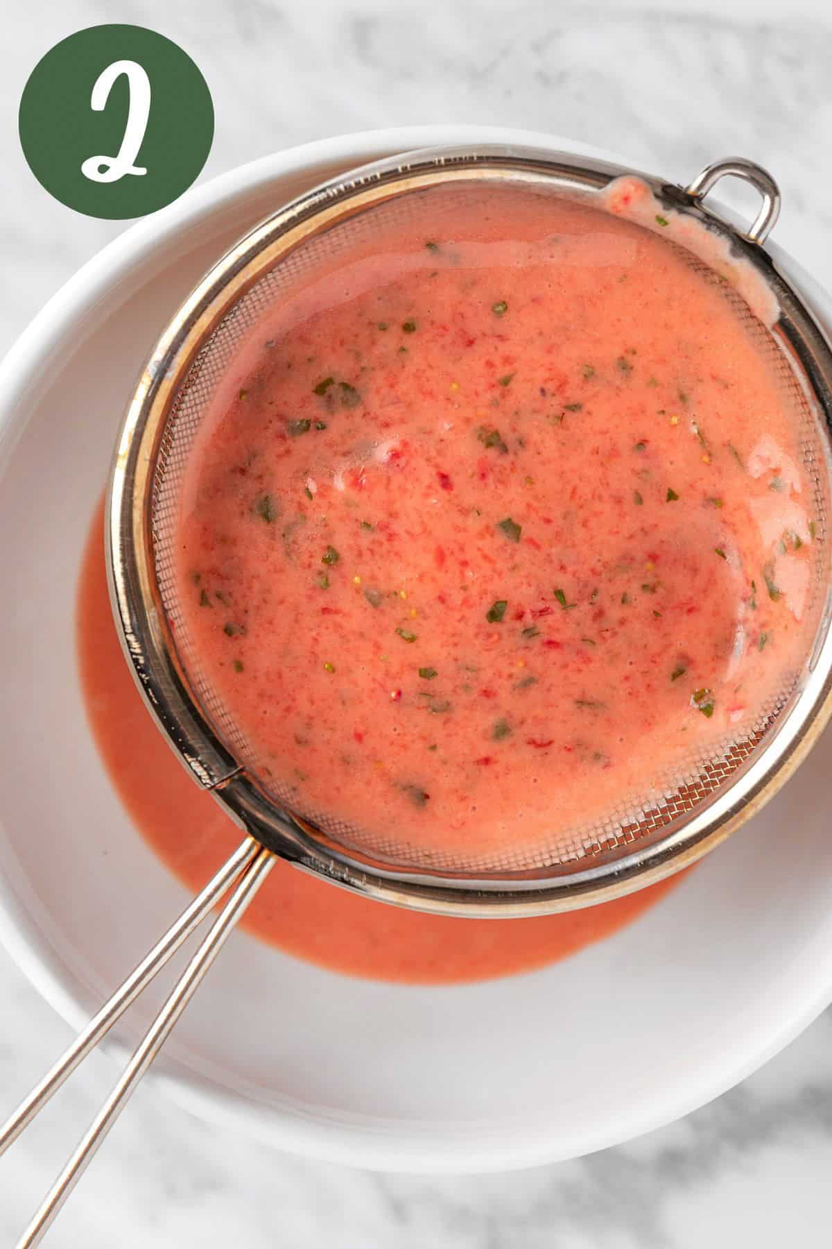 Overhead view of a strainer being used to strain the strawberry dressing.