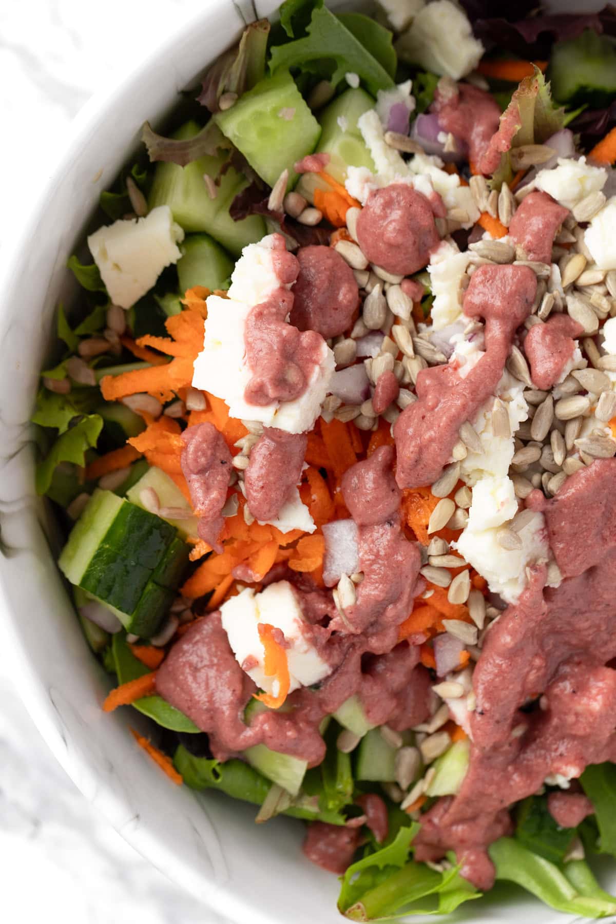 A green salad with carrots, cucumbers, feta and sunflower seeds, topped with blueberry dressing.