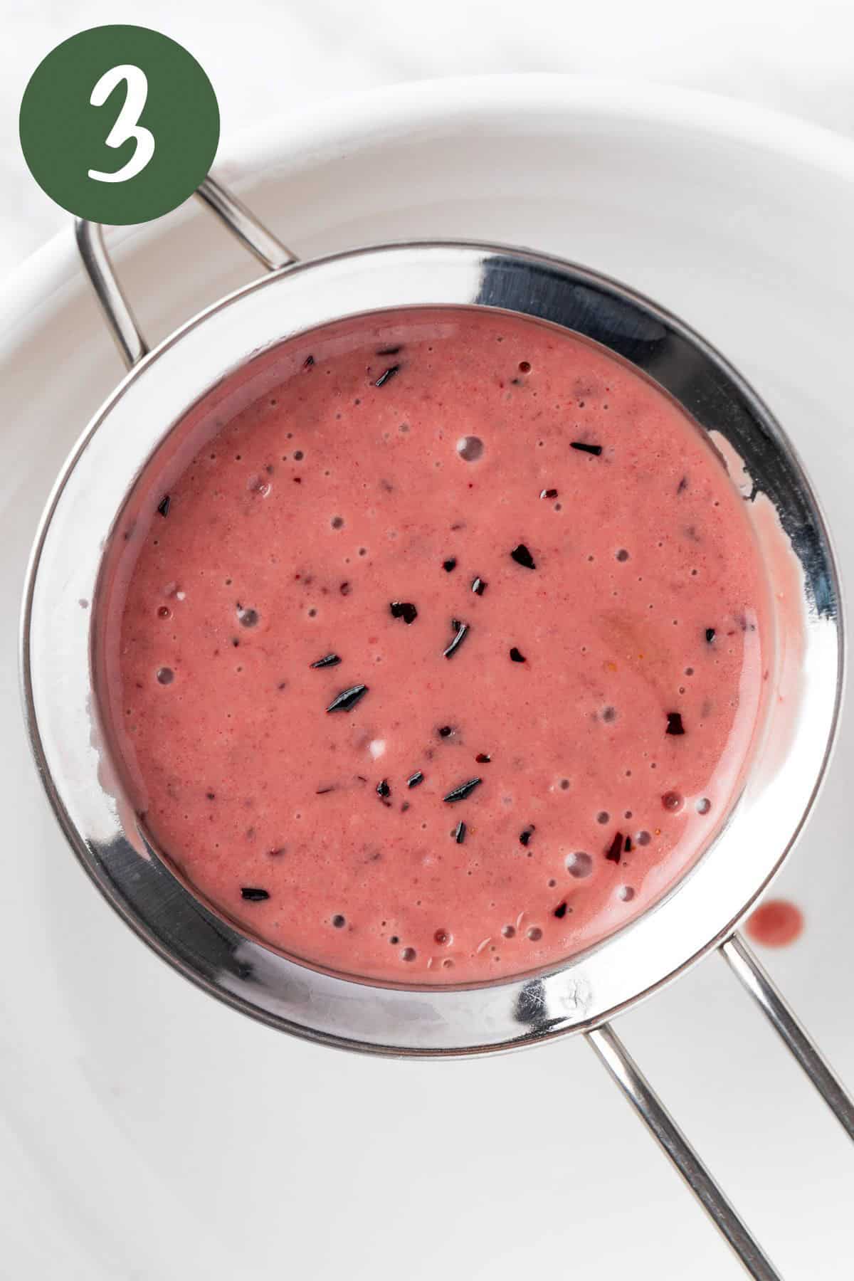 Straining the blueberry dressing with a fine mesh sieve.