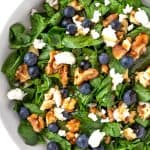 Blueberry goat cheese salad with spinach and toasted walnuts in a white bowl, topped with a maple dressing.