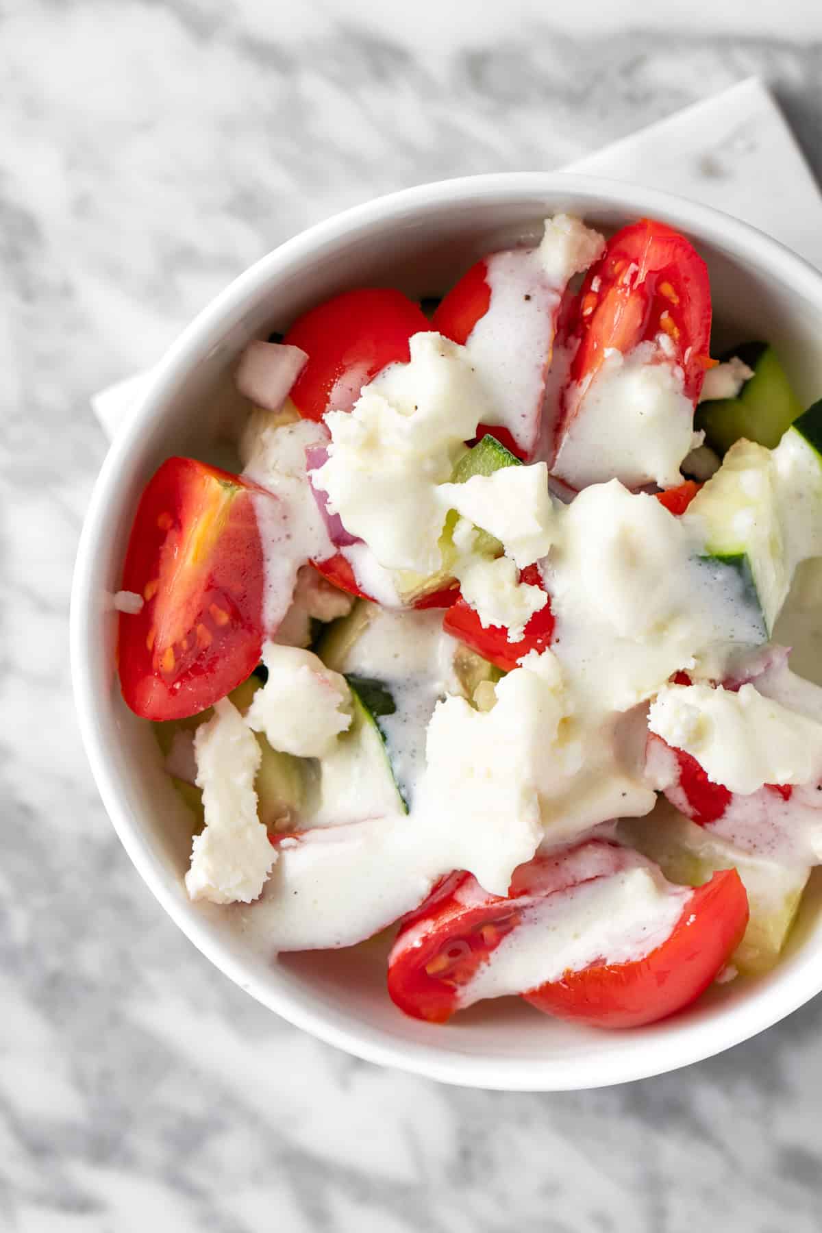 A salad with feta, tomatoes, and cucumbers, topped with the white tzatziki dressing.