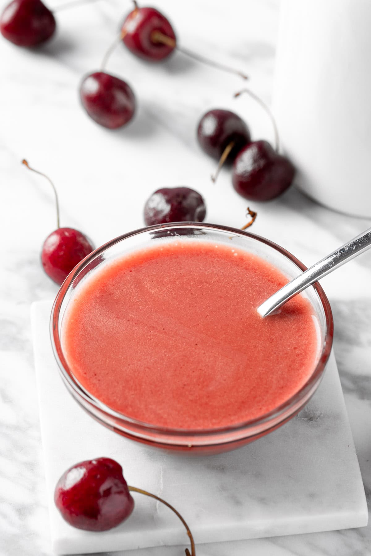 A small bowl of cherry balsamic vinaigrette on a white table next to fresh cherries.
