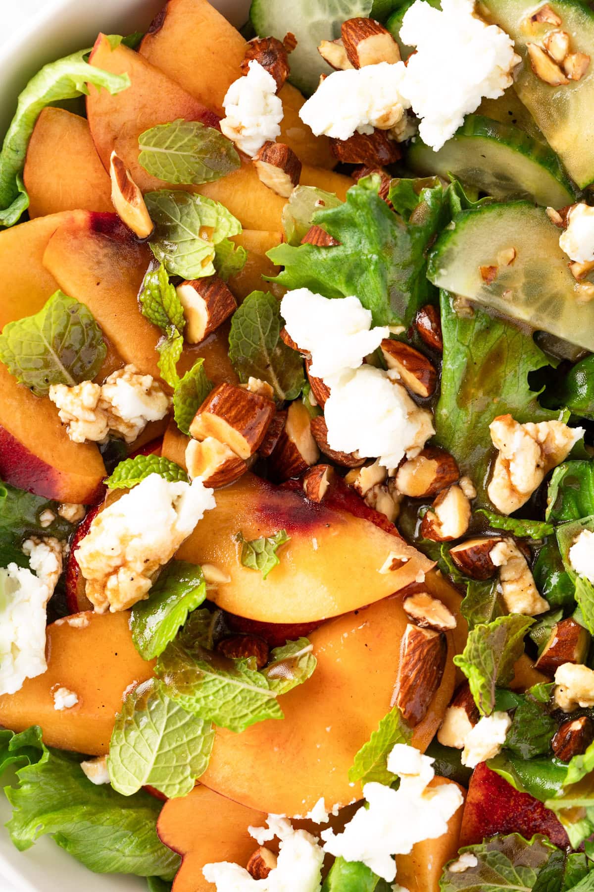 A peach and goat cheese salad with chopped almonds, mint leaves, basil leaves and cucumber.