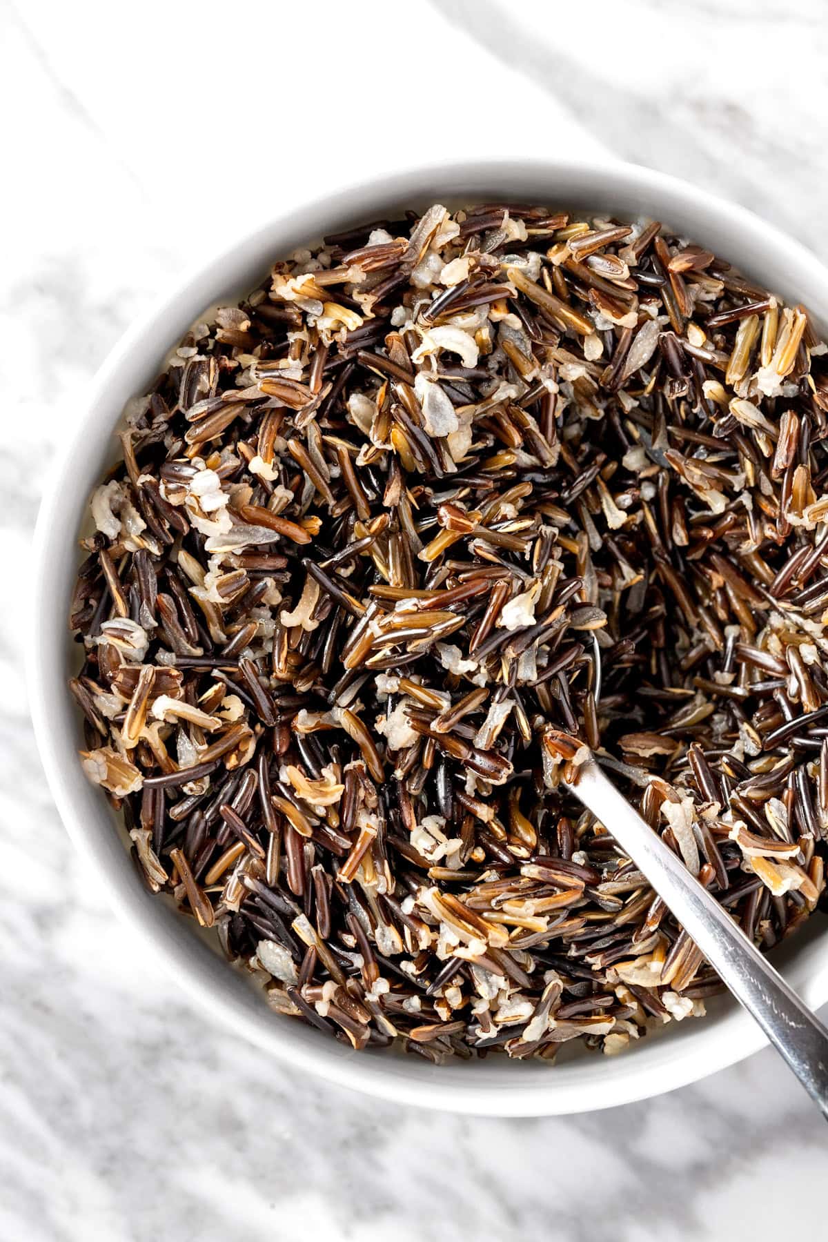 A bowl of wild rice on a white marble table.