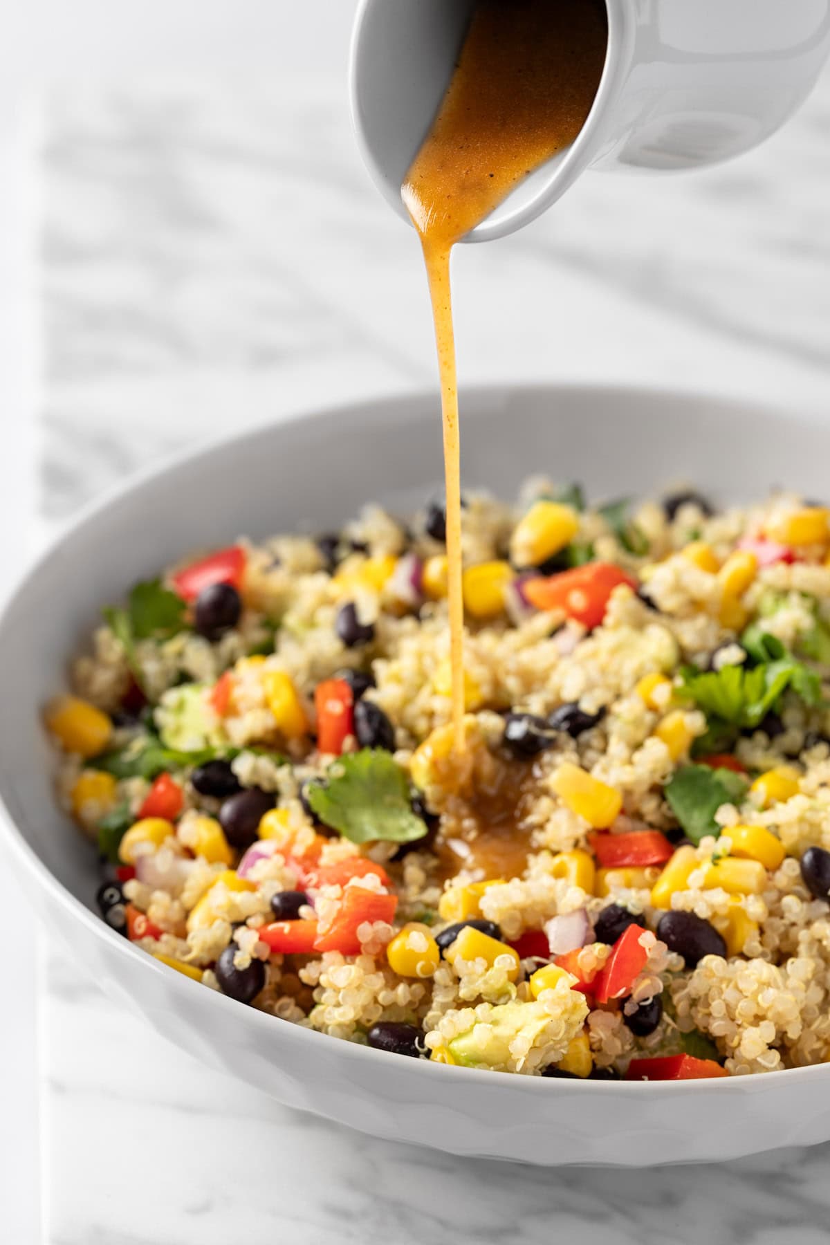 Pouring the chili lime vinaigrette over a quinoa salad with corns, black beans and red peppers.