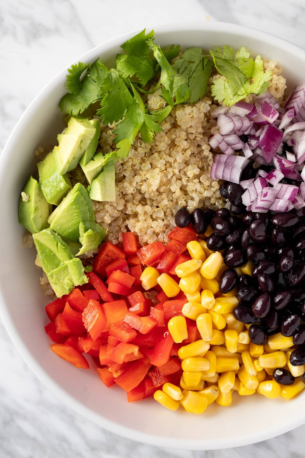 A bowl of salad made with quinoa, corn, black beans, red pepper, red onion and avocado.