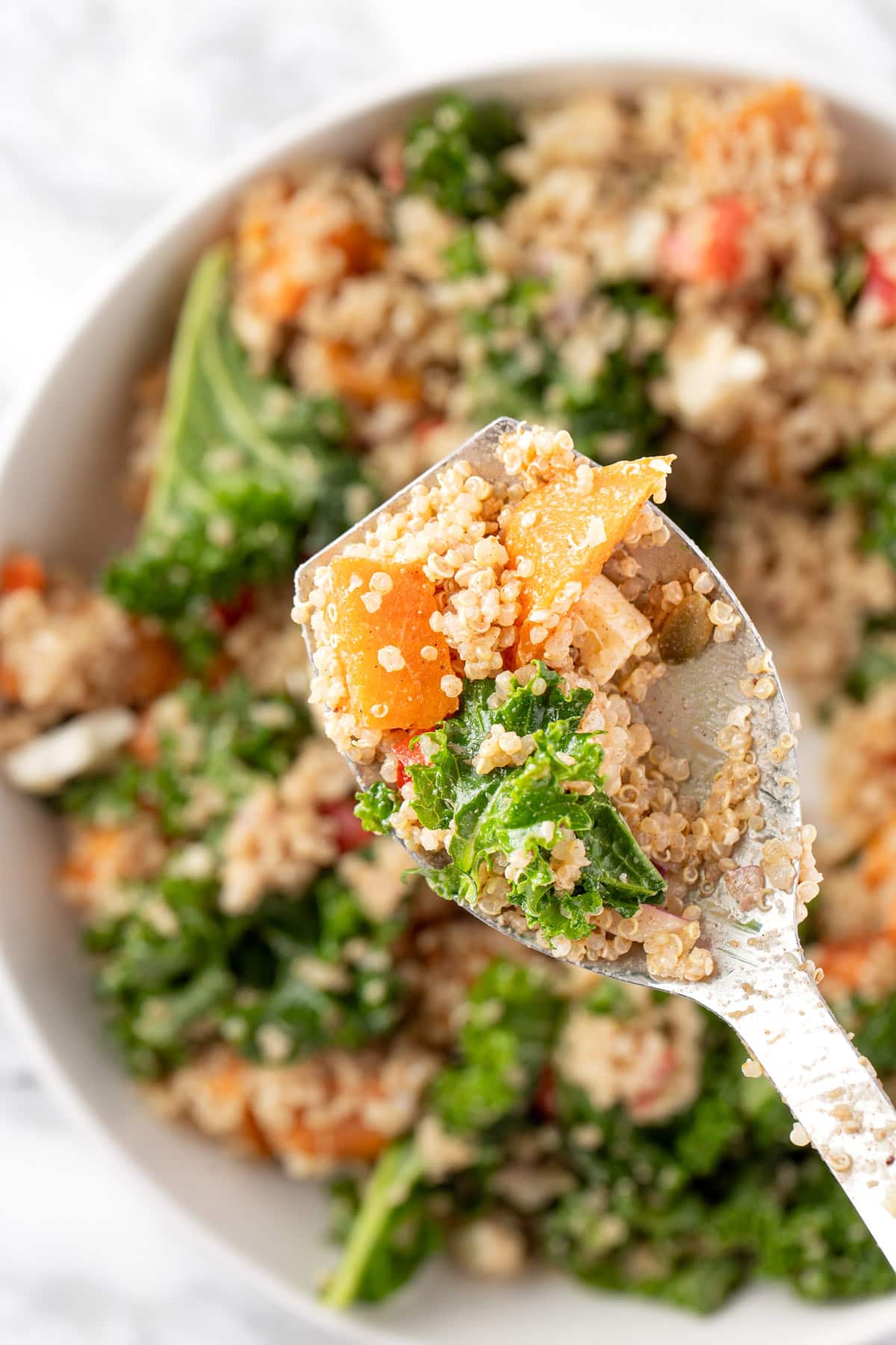 An up-close spoonful of sweet potato quinoa salad with kale and feta, topped with a balsamic date vinaigrette.