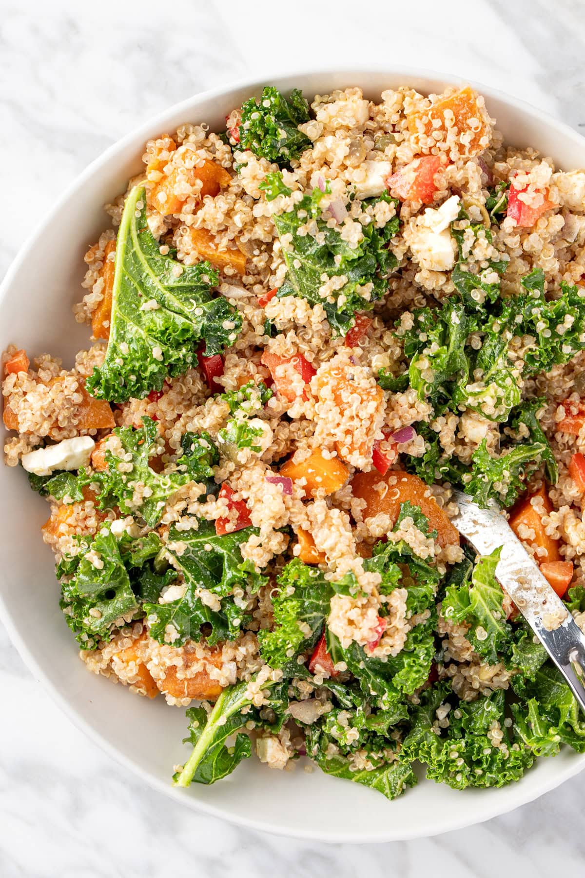 A bowl of sweet potato quinoa salad with red bell pepper, kale, feta and red onion.