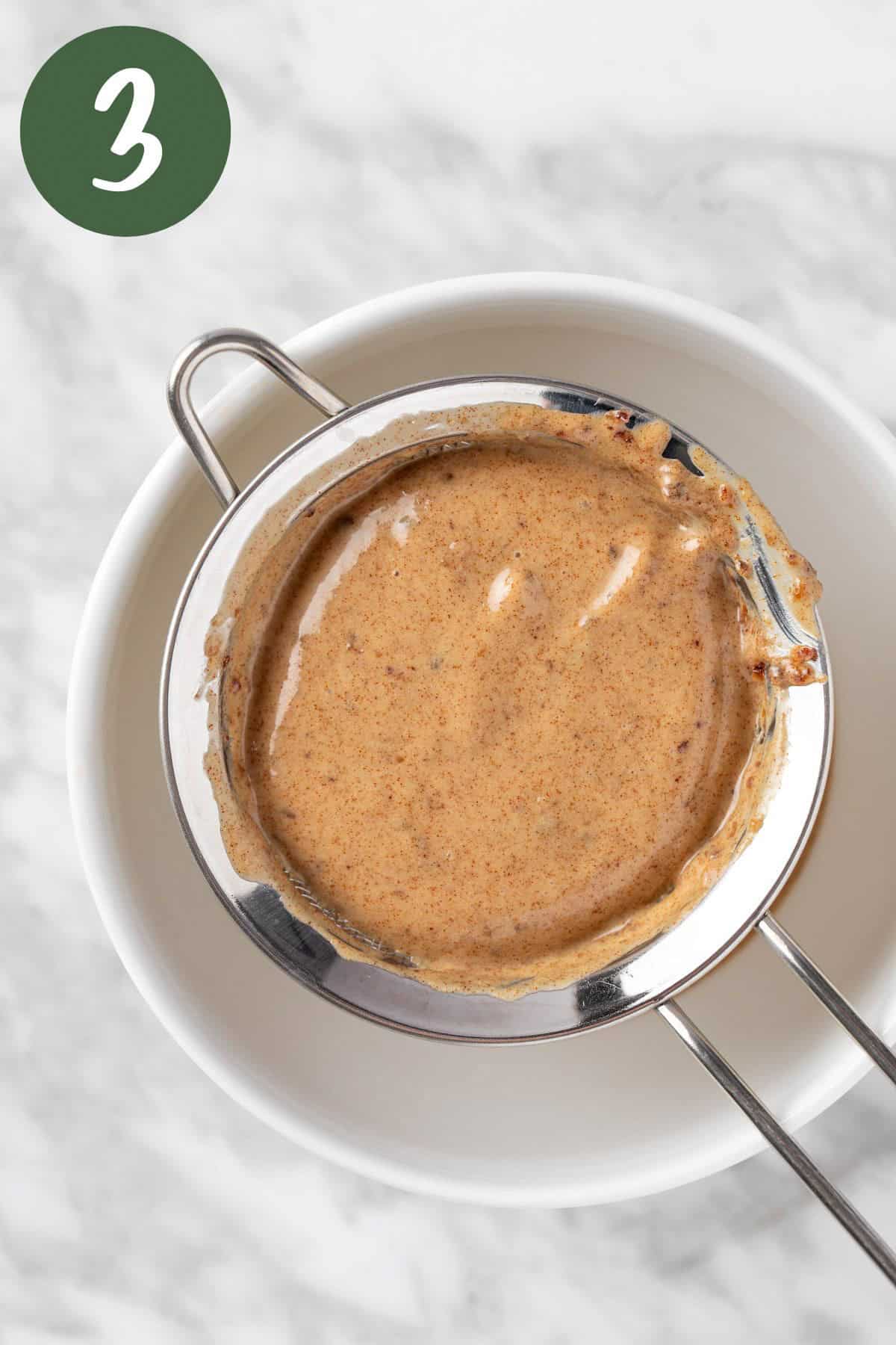Straining the balsamic date vinaigrette through a fine mesh sieve into a white bowl.
