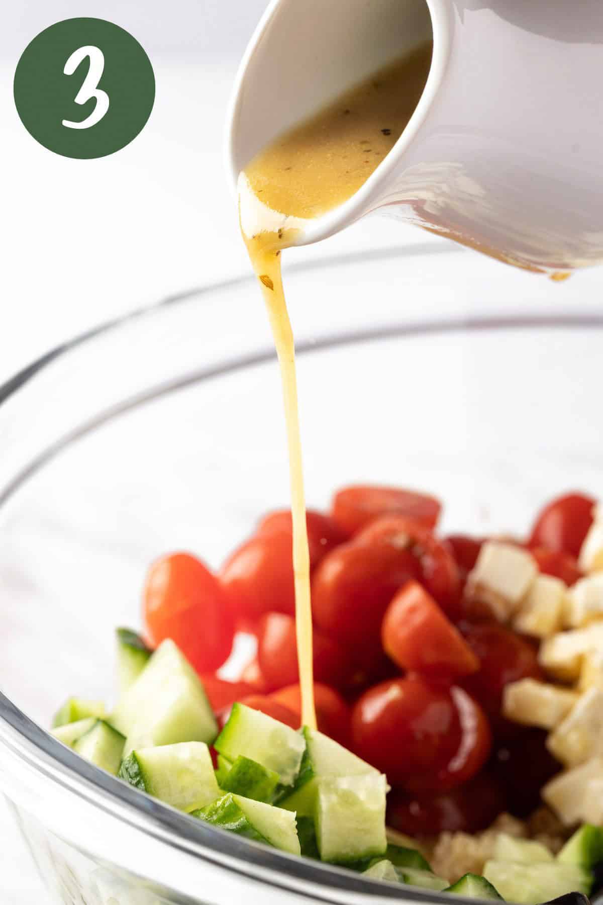 Pouring the red wine vinaigrette over top of the Greek Quinoa Salad.