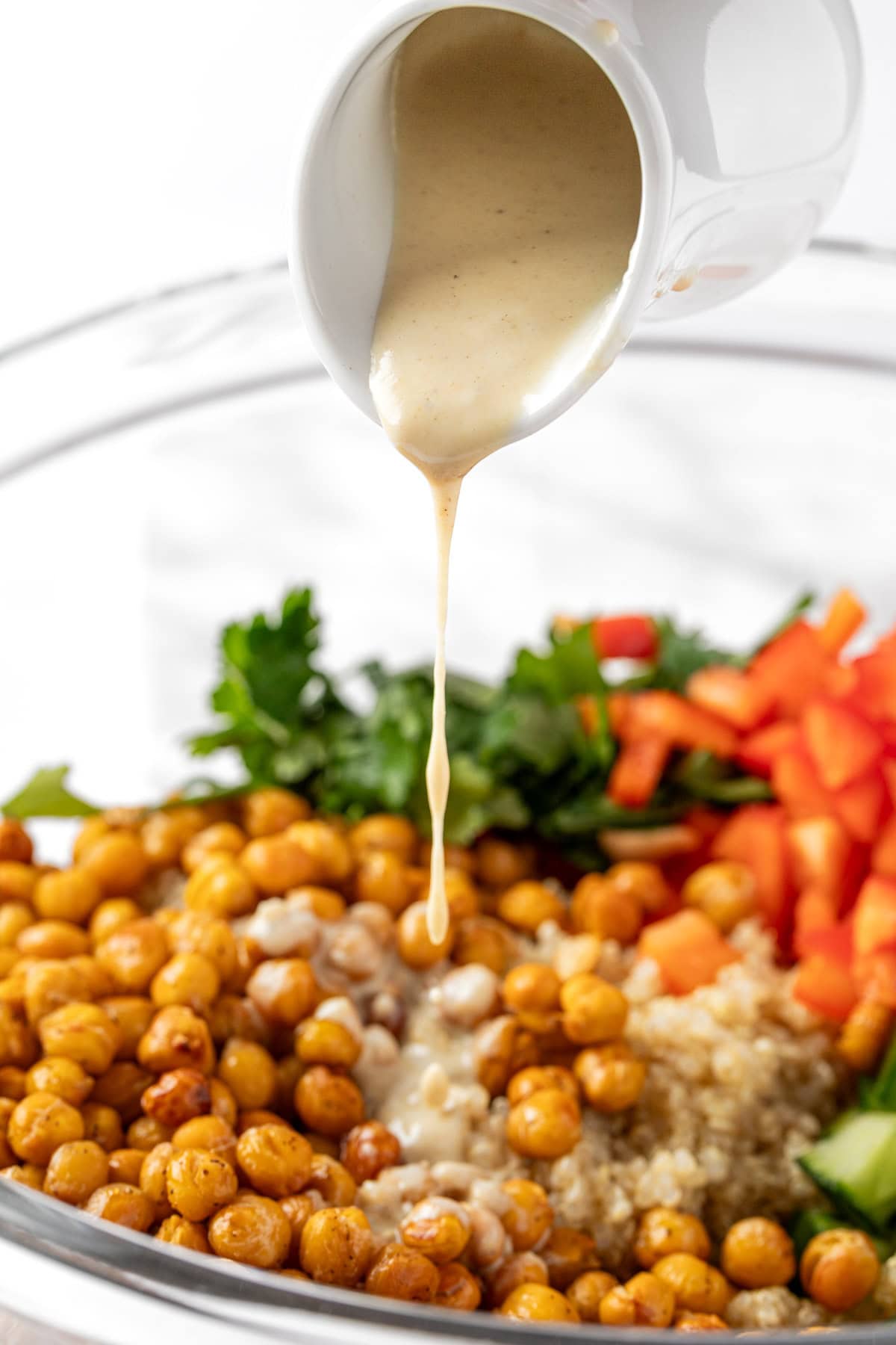 Pouring the lemon tahini dressing over a salad made with roasted chickpeas, quinoa, parsley and peppers.