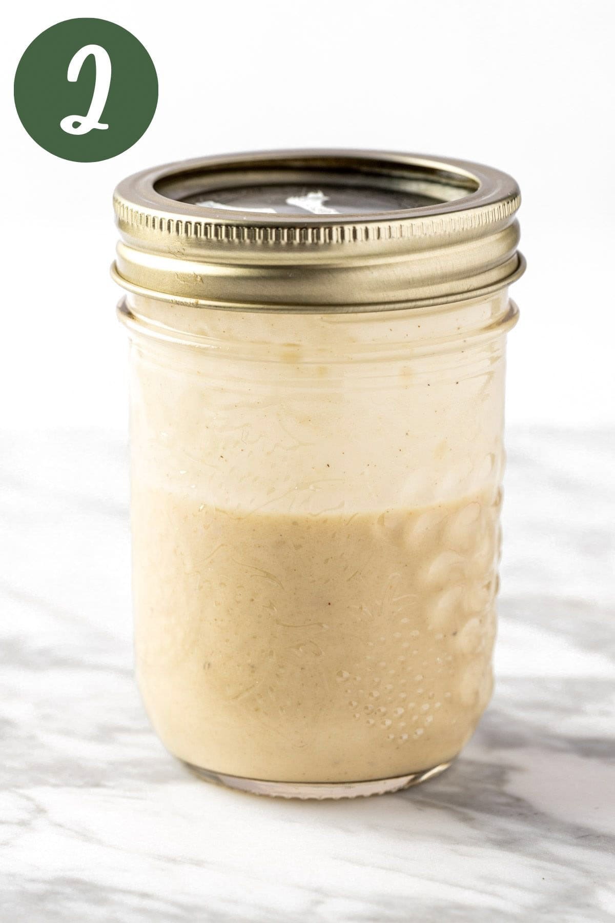 A process photo of the lemon tahini dressing shaken in a mason jar.