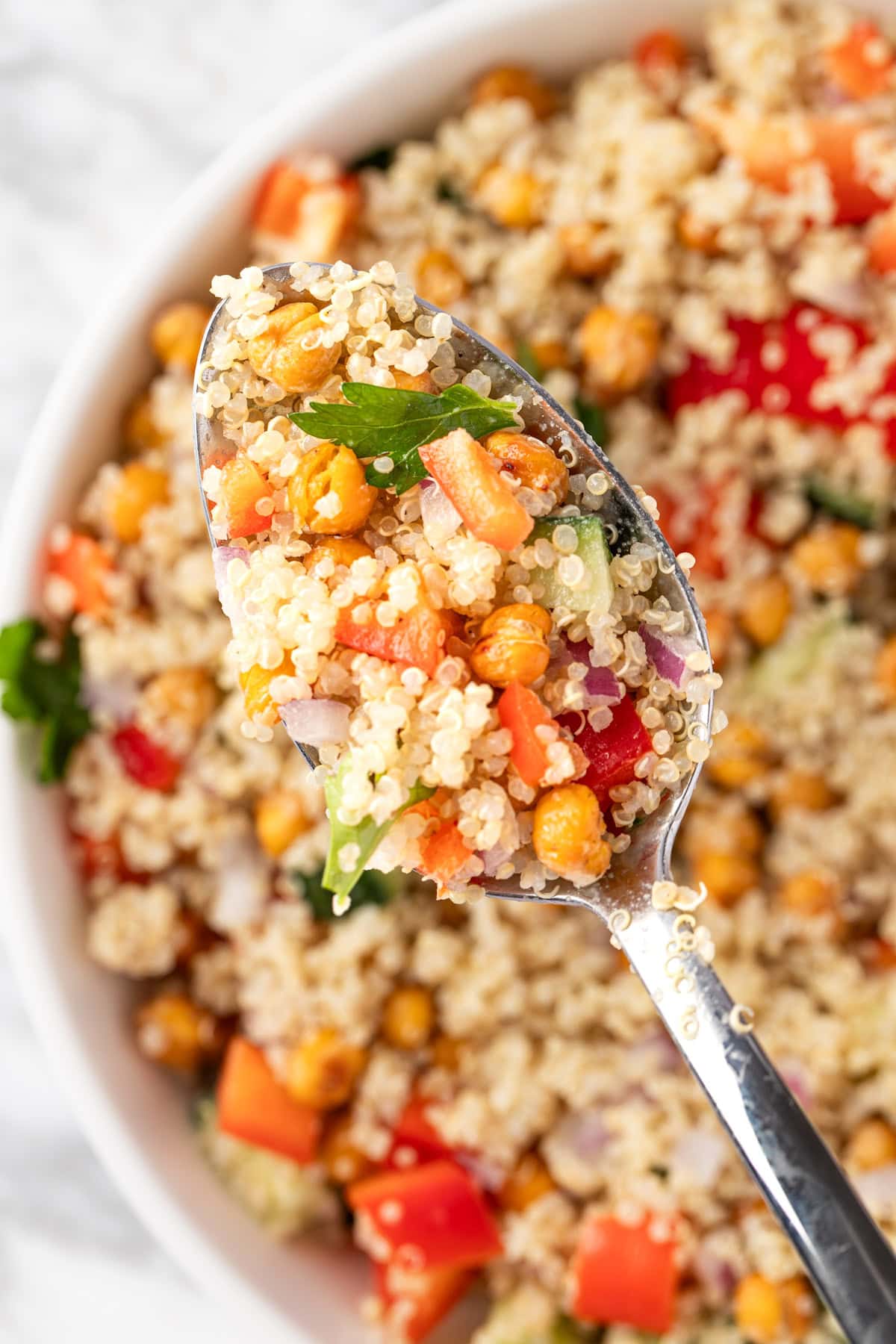An up close view of a spoonful of chickpea quinoa salad made with roasted chickpeas, bell peppers, cucumber, red onion, parsley and a lemon tahini dressing.
