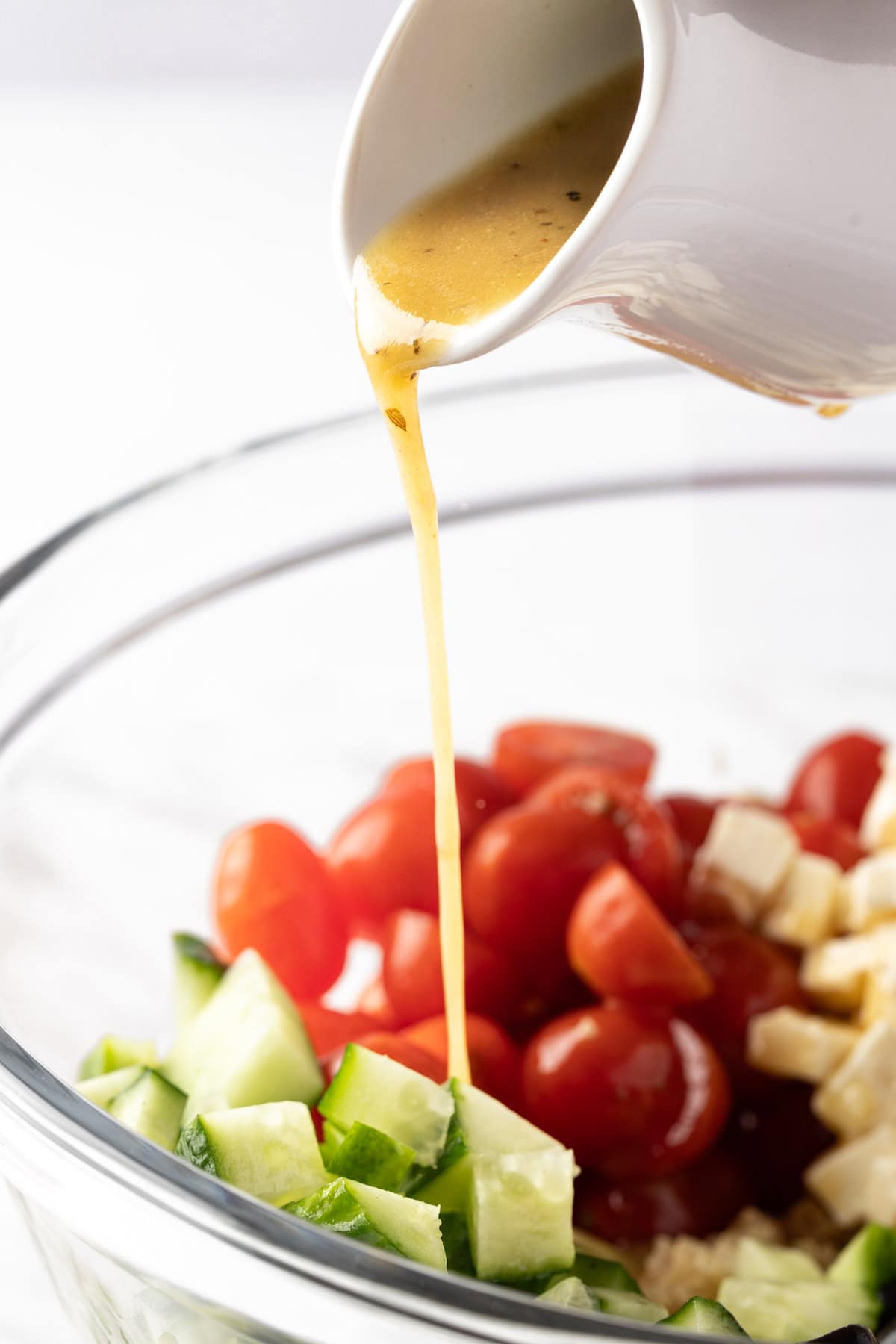 Pouring the red wine vinaigrette over a green salad with cucumbers and tomatoes.