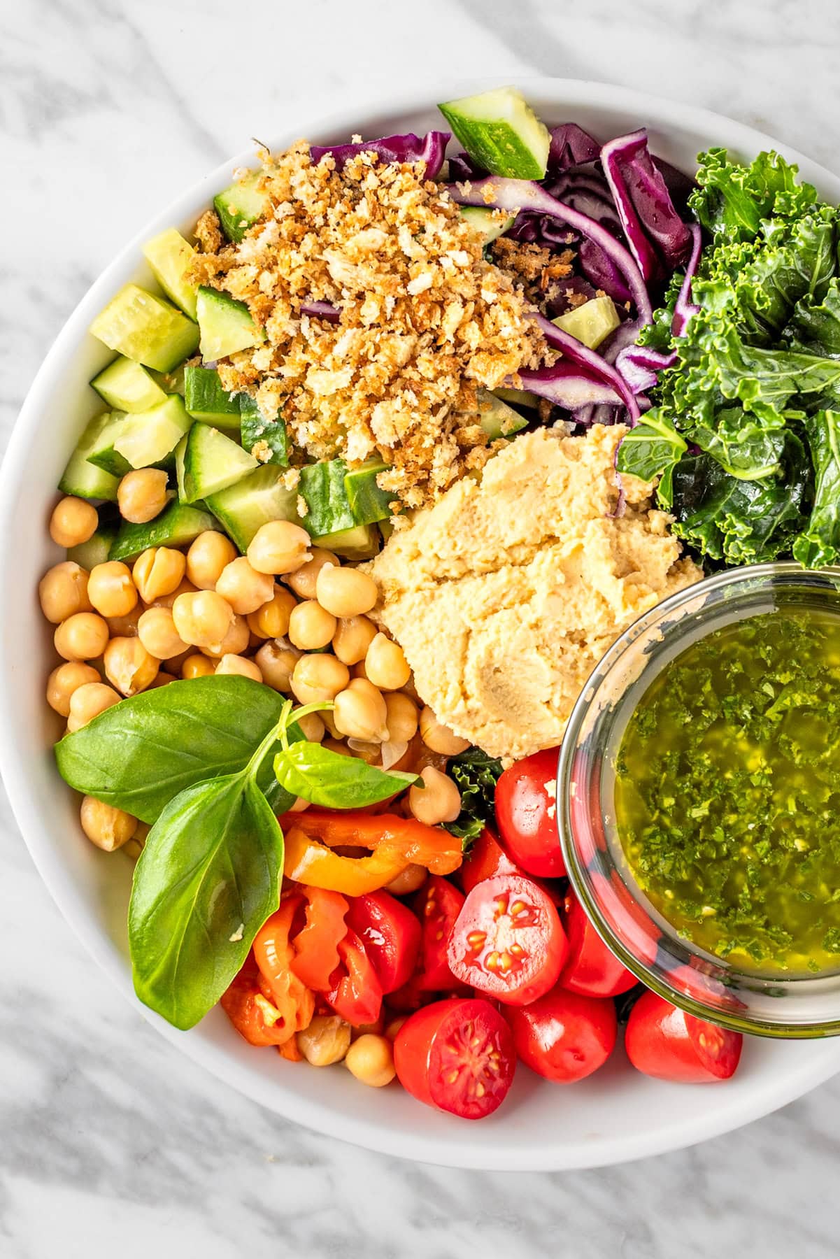 A bowl of Sweetgreen Hummus Crunch salad made with cherry tomatoes, chickpeas, basil leaves, kale, red cabbage, cucumbers, za’atar bread crumbs, hummus and pesto vinaigrette.