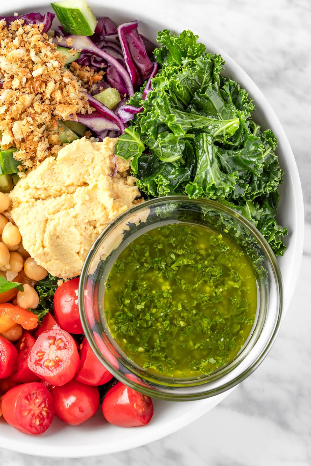 A bowl of Sweetgreen Hummus Crunch salad made with cherry tomatoes, chickpeas, basil leaves, kale, red cabbage, cucumbers, za’atar bread crumbs, hummus and pesto vinaigrette.