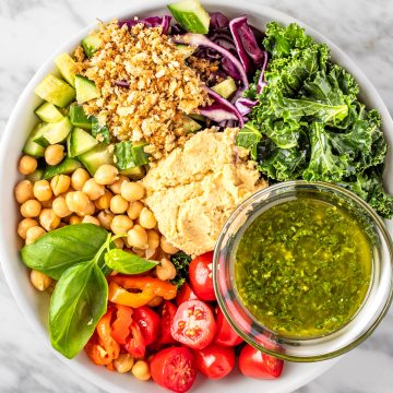 A bowl of Sweetgreen Hummus Crunch salad made with cherry tomatoes, chickpeas, basil leaves, kale, red cabbage, cucumbers, za’atar bread crumbs, hummus and pesto vinaigrette.