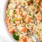 An up close view of a spoonful of Quinoa Tabbouleh Salad with diced tomatoes, mint leaves and parsley.