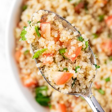 An up close view of a spoonful of Quinoa Tabbouleh Salad with diced tomatoes, mint leaves and parsley.