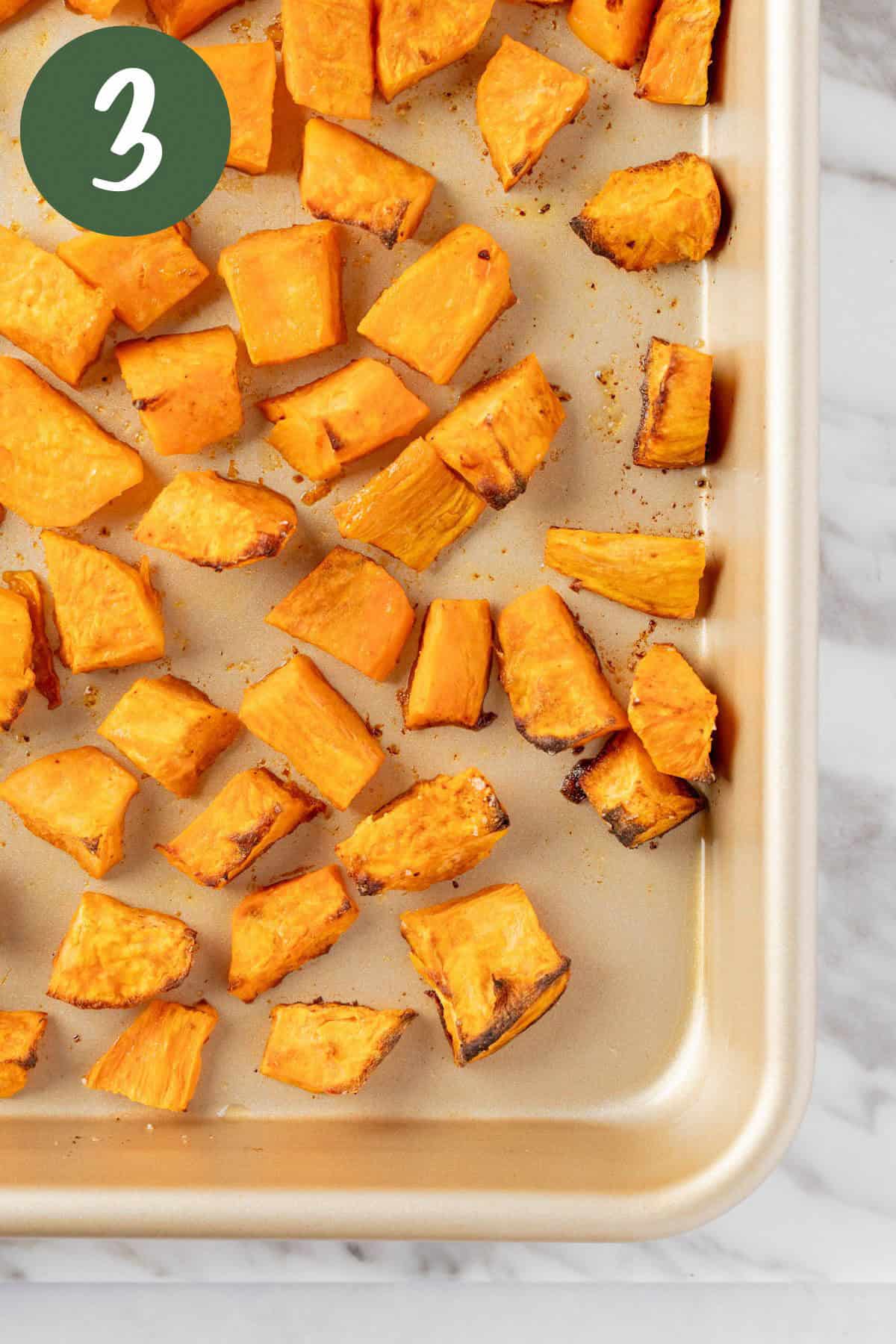 A baking sheet of roasted Sweetgreen sweet potatoes on a white marble table.