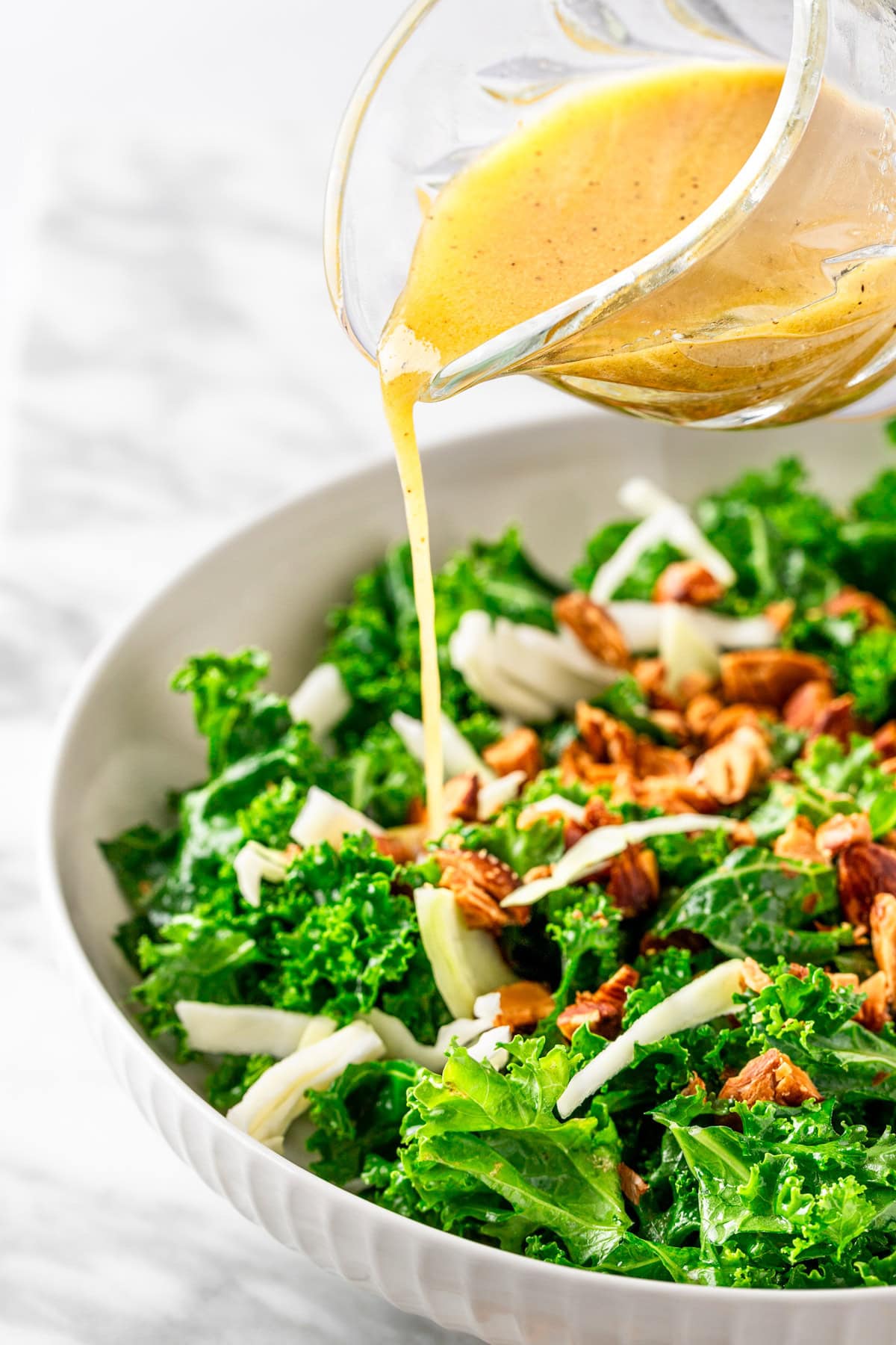 Pouring the apple cider dijon mustard vinaigrette over a salad with kale, roasted almonds and green cabbage.
