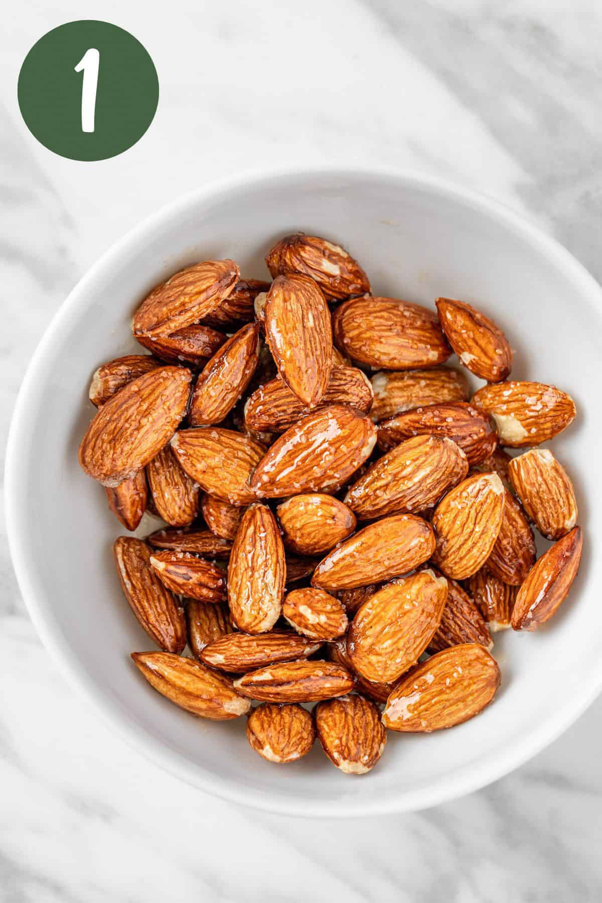 A process photo of the almonds seasoned with olive oil and sea salt in a white bowl.