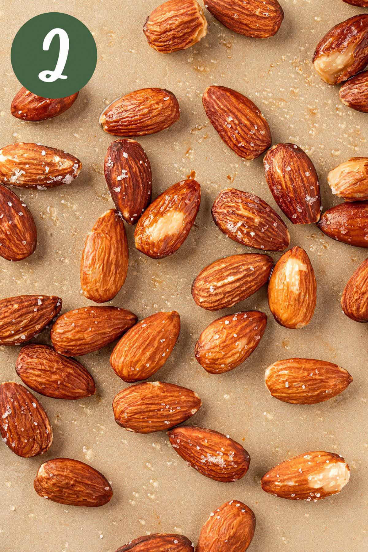 A process photo of roasted salted almonds on a baking sheet fresh out of the oven.