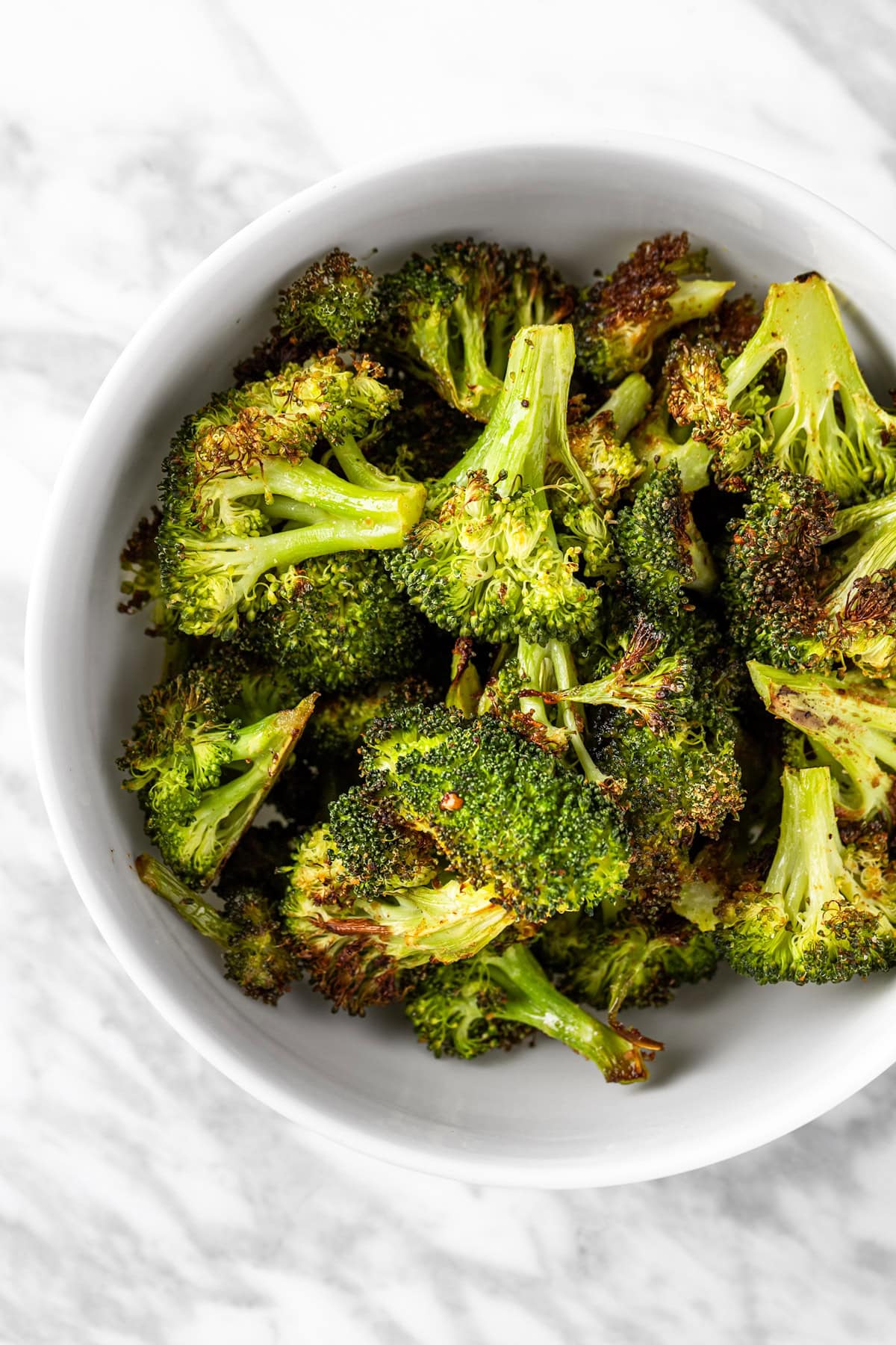 A bowl of spicy Sweetgreen broccoli on a white marble table.
