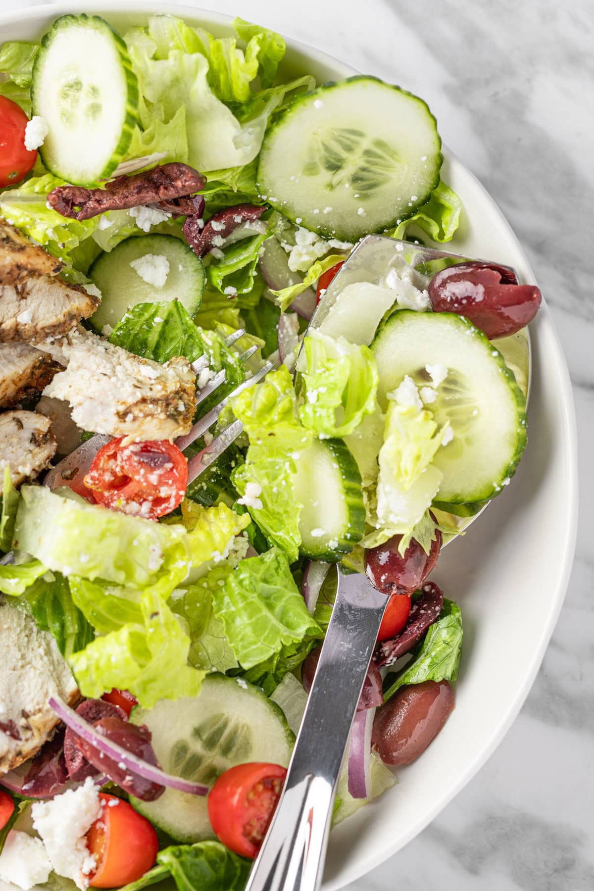 A bowl of Panera Greek Salad with a metal serving spoon.