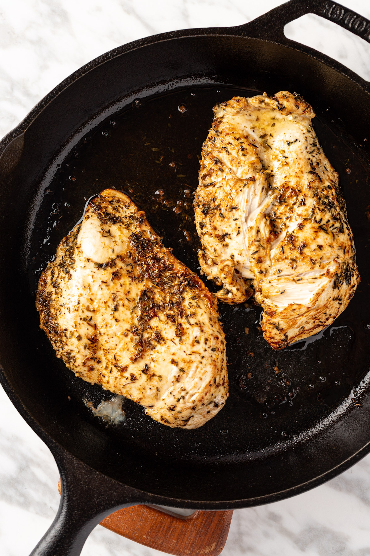 A couple of cooked chicken breasts in a cast iron pan.