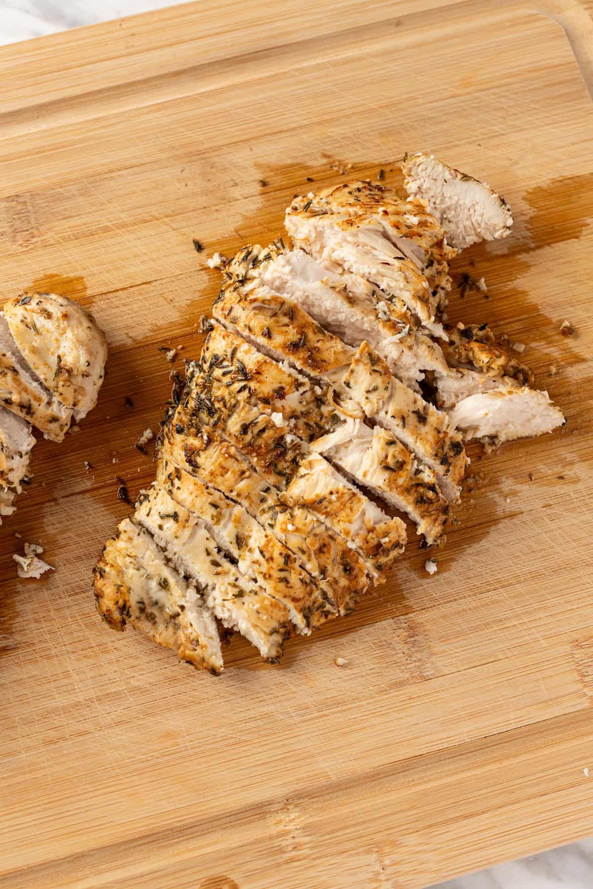 A cooked chicken breast on a wooden cutting board, sliced into long strips for salad.