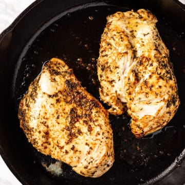 A couple of cooked chicken breasts in a cast iron pan.