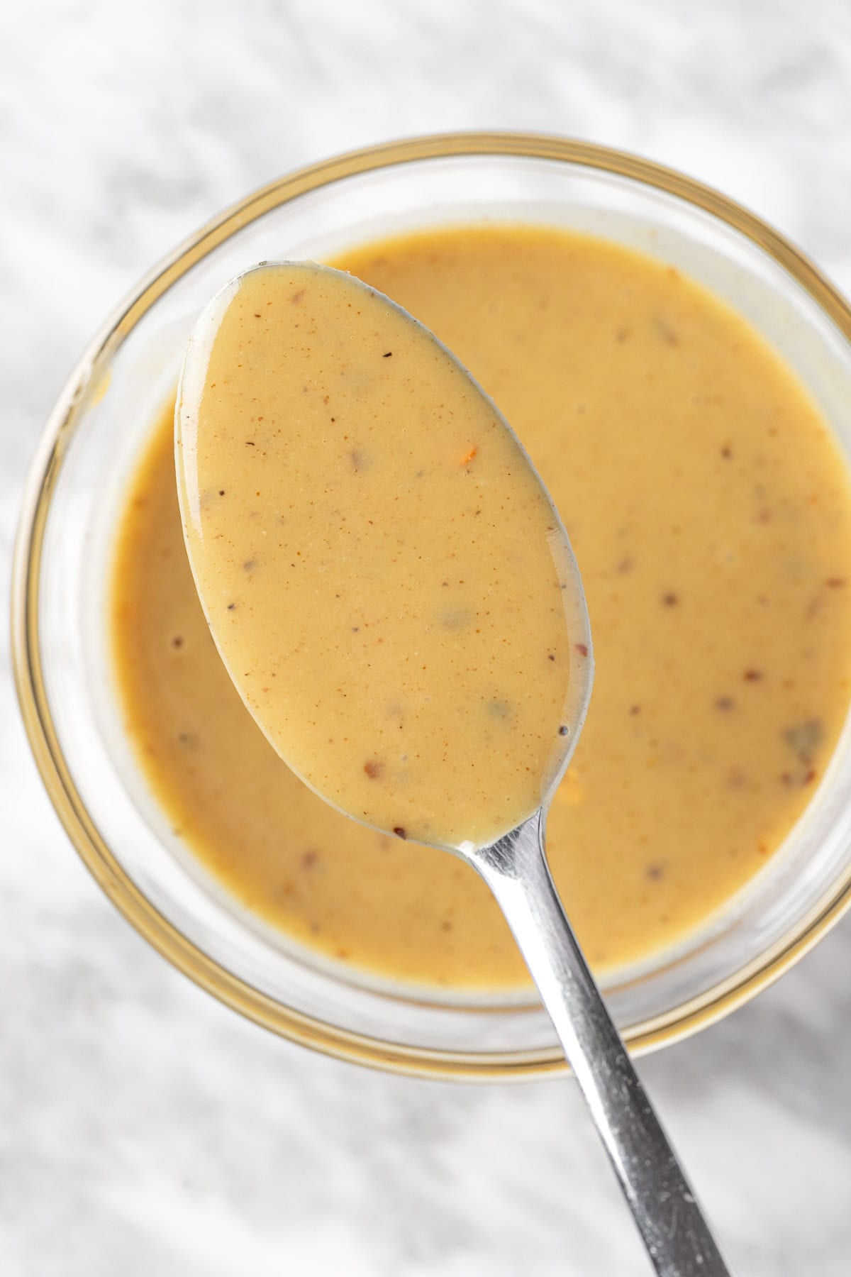 A close up view of a spoonful of yellow hot honey mustard sauce.
