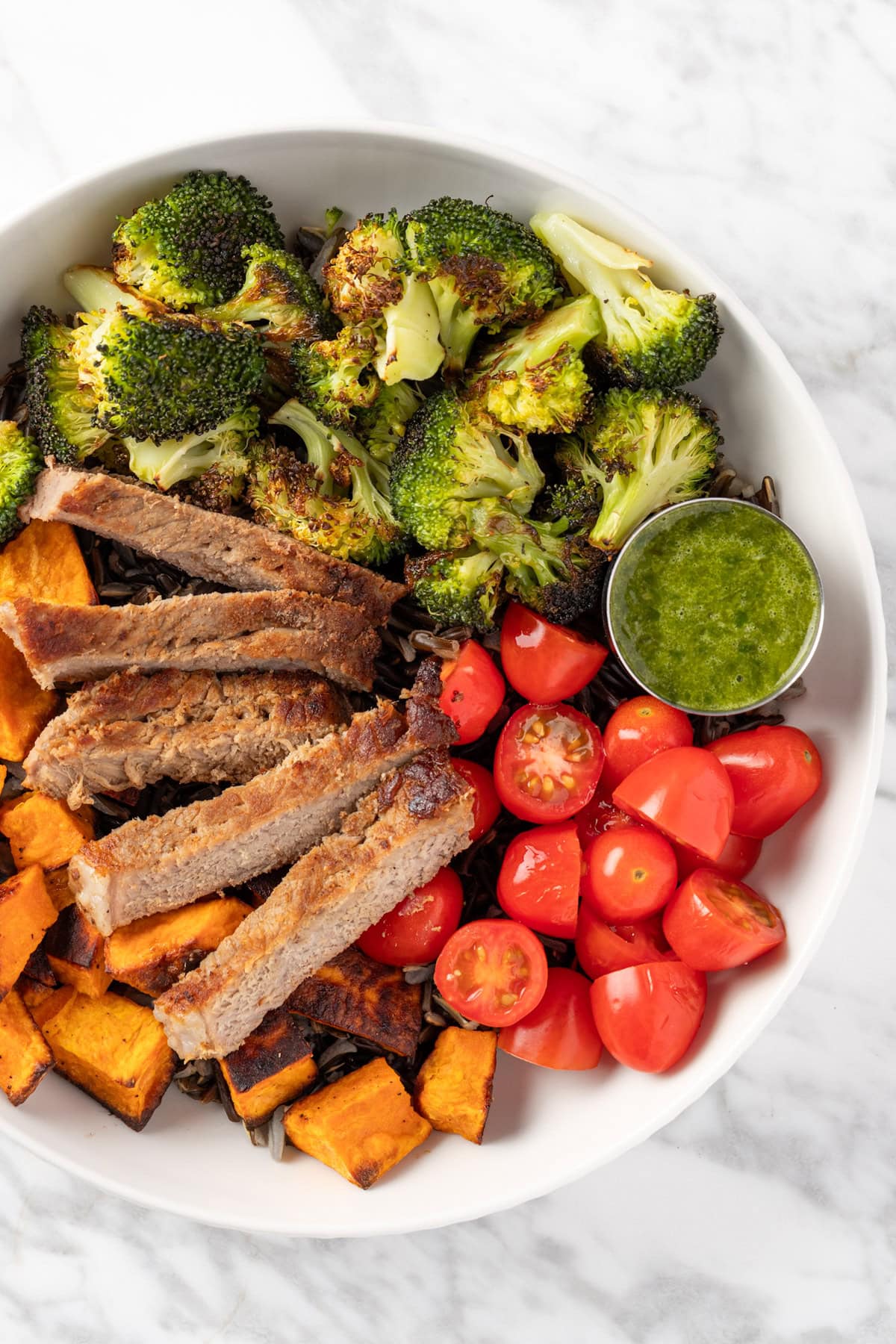 Overhead view of Sweetgreen Caramelized Steak Plate with steak, cherry tomatoes, sweet potatoes, wild rice and pesto vinaigrette.